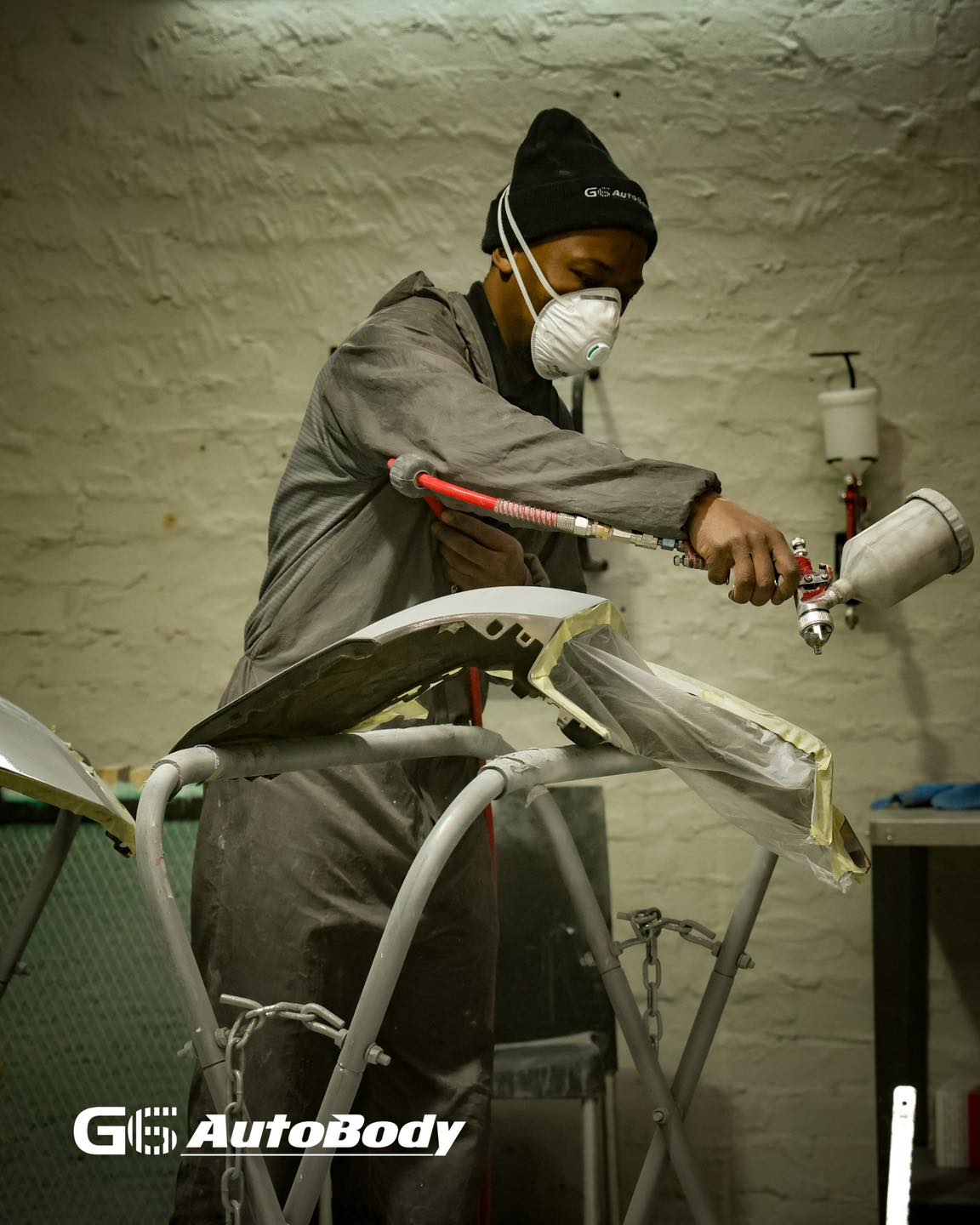 G6 AutoBody painter in full respirator spraying a masked bumper